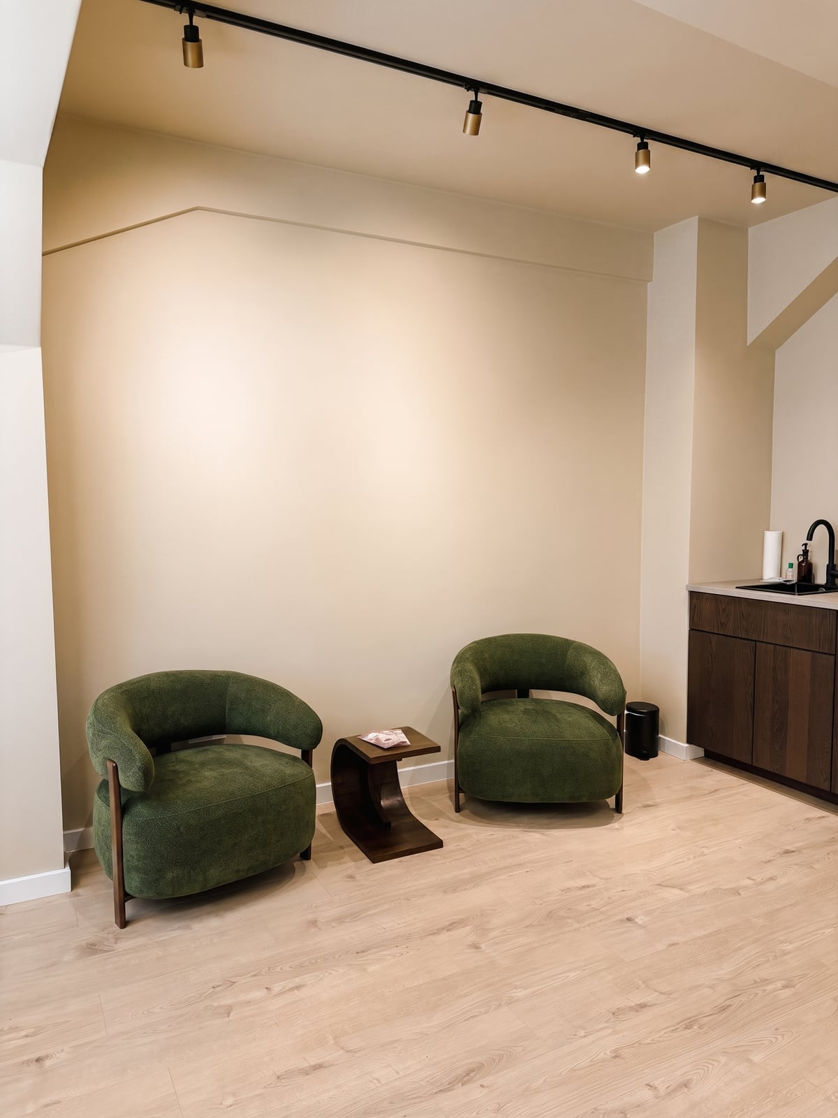 Wartebereich im Studio von Aurea Aesthetics mit grünen Sesseln und hellem Holzboden
